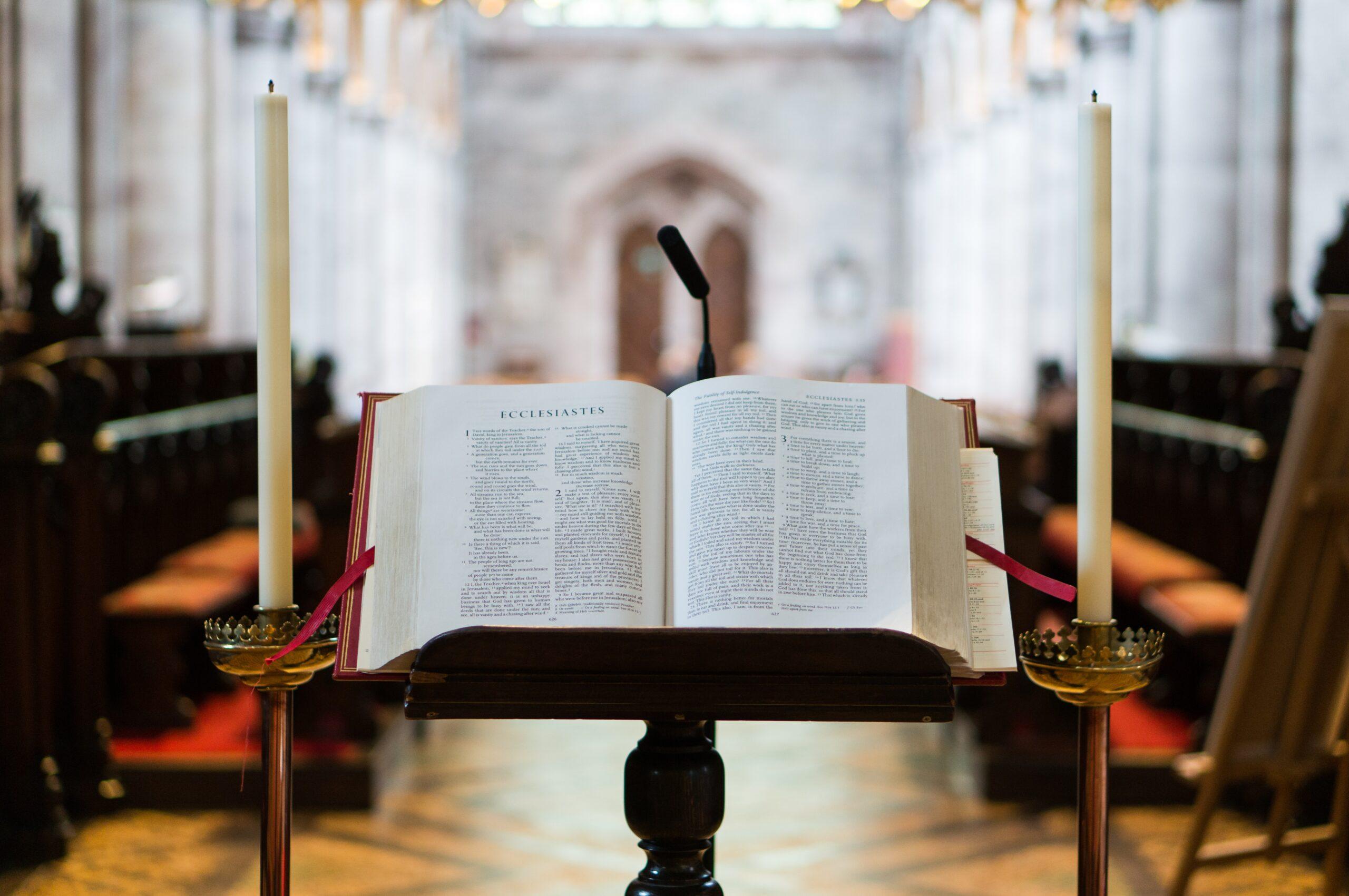 Open Bible resting on a lectern between two candles.